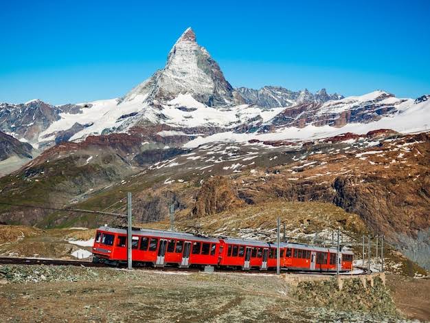 The open-air Gornergrat train ascending a ridge with a clear view of the Matterhorn in summer.