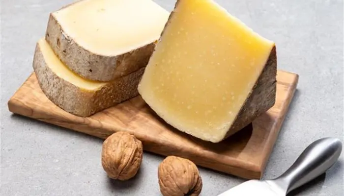 A wedge of firm Comté cheese with a natural brown rind and pale yellow interior displayed on a wooden board."