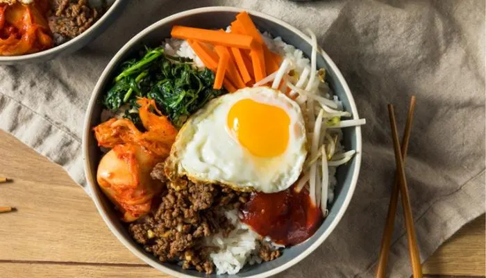 A traditional Korean bibimbap bowl with assorted colorful vegetables, beef, and a sunny-side-up egg.