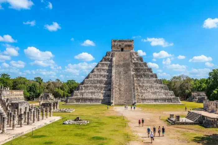 The iconic El Castillo pyramid at Chichen Itza under a bright blue sky with surrounding Mayan ruins.