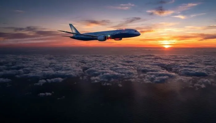 A commercial airliner flying above the clouds at sunset over a vast dark ocean
